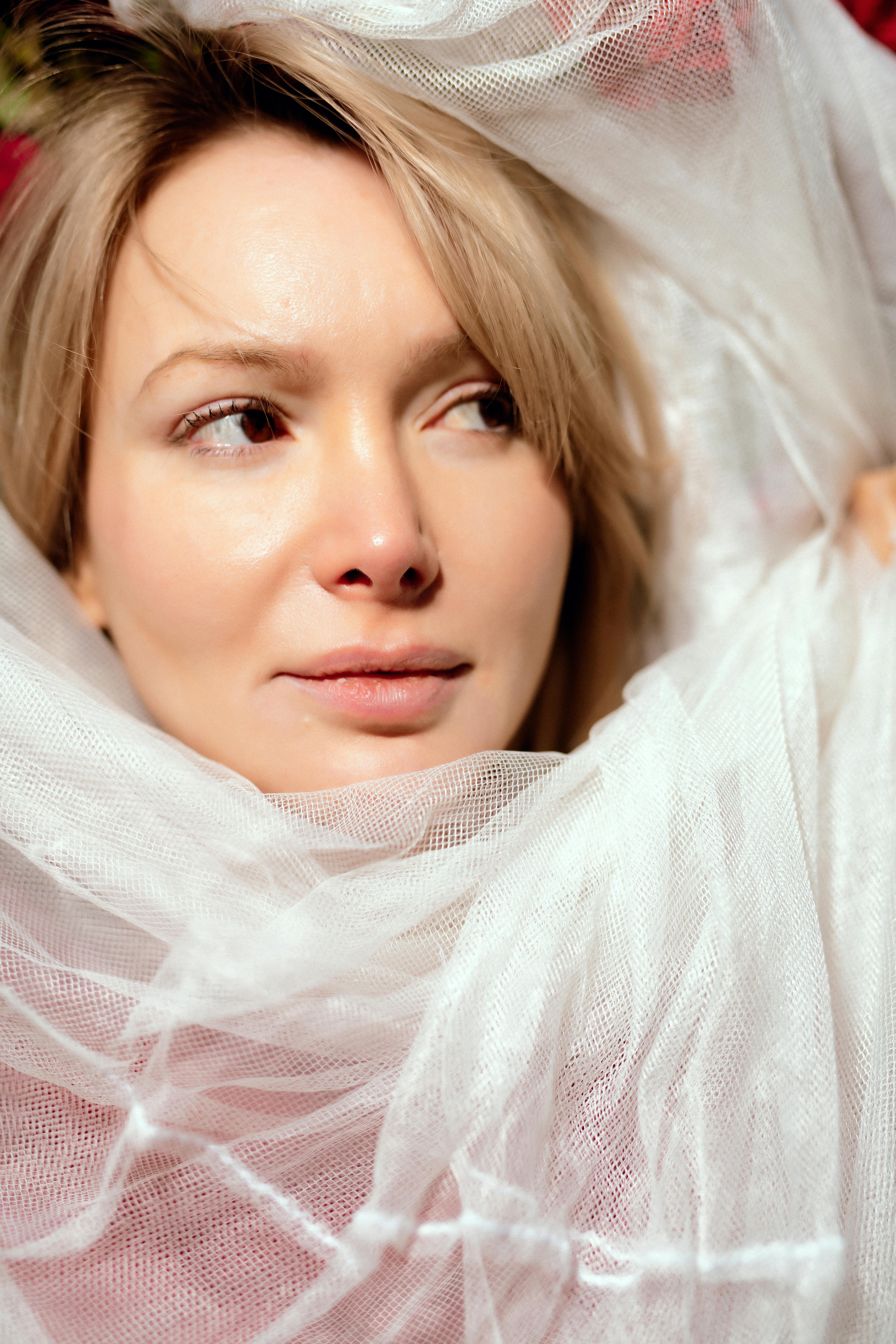 Ilmainen Muotokuva naisesta, joka on taiteellisesti verhoiltu pehmeään valkoiseen tylliin, välittäen mysteerin ja eleganssin tunnetta. Kuvapankkikuva
