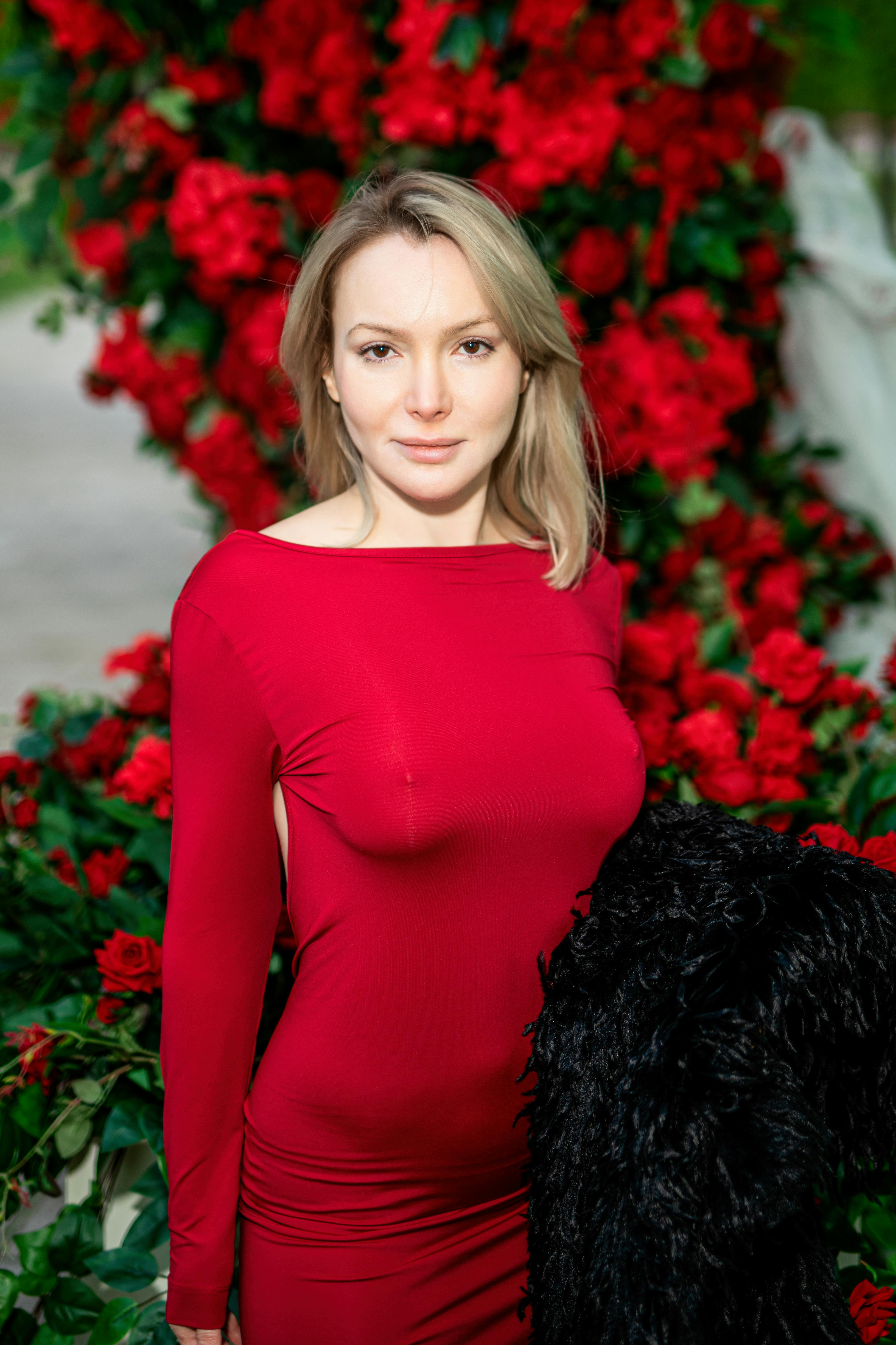 бесплатная Женщина в красном платье позирует с яркими красными розами, излучая элегантность и стиль. Стоковое фото