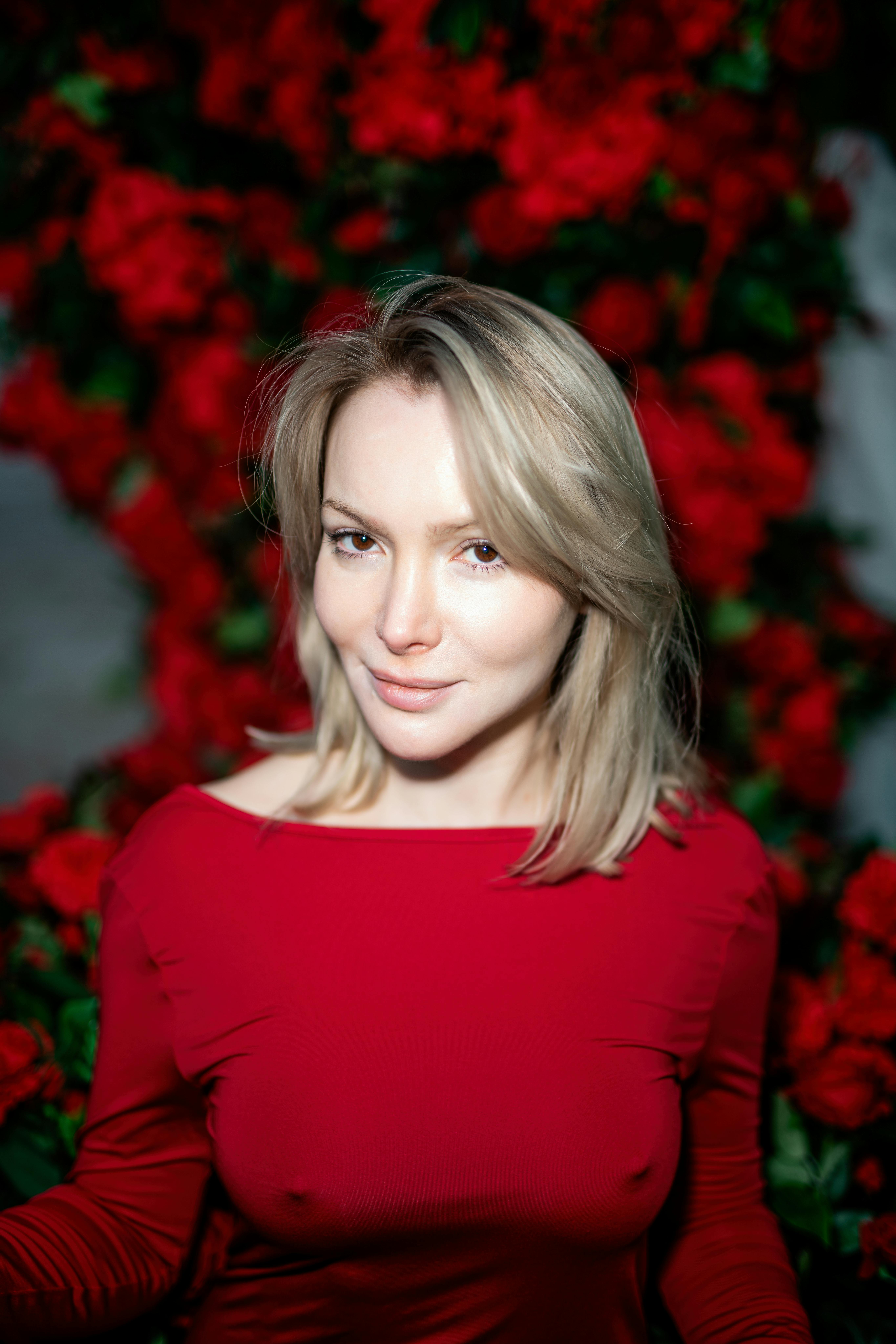 Kostnadsfria Porträtt av en blond kvinna i rött omgiven av livfulla röda rosor, som utstrålar elegans och charm. Stock foto