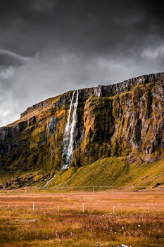 在阴沉的天空下，一道戏剧性的瀑布沿着岩石悬崖倾泻而下，四周环绕着郁郁葱葱的绿色植物