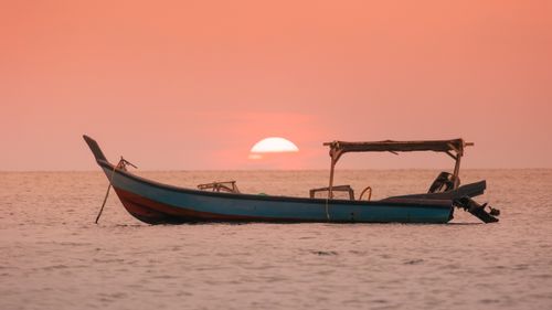 Free A serene boat floats on Pangkor Island's waters against a vibrant sunset backdrop. Stock Photo