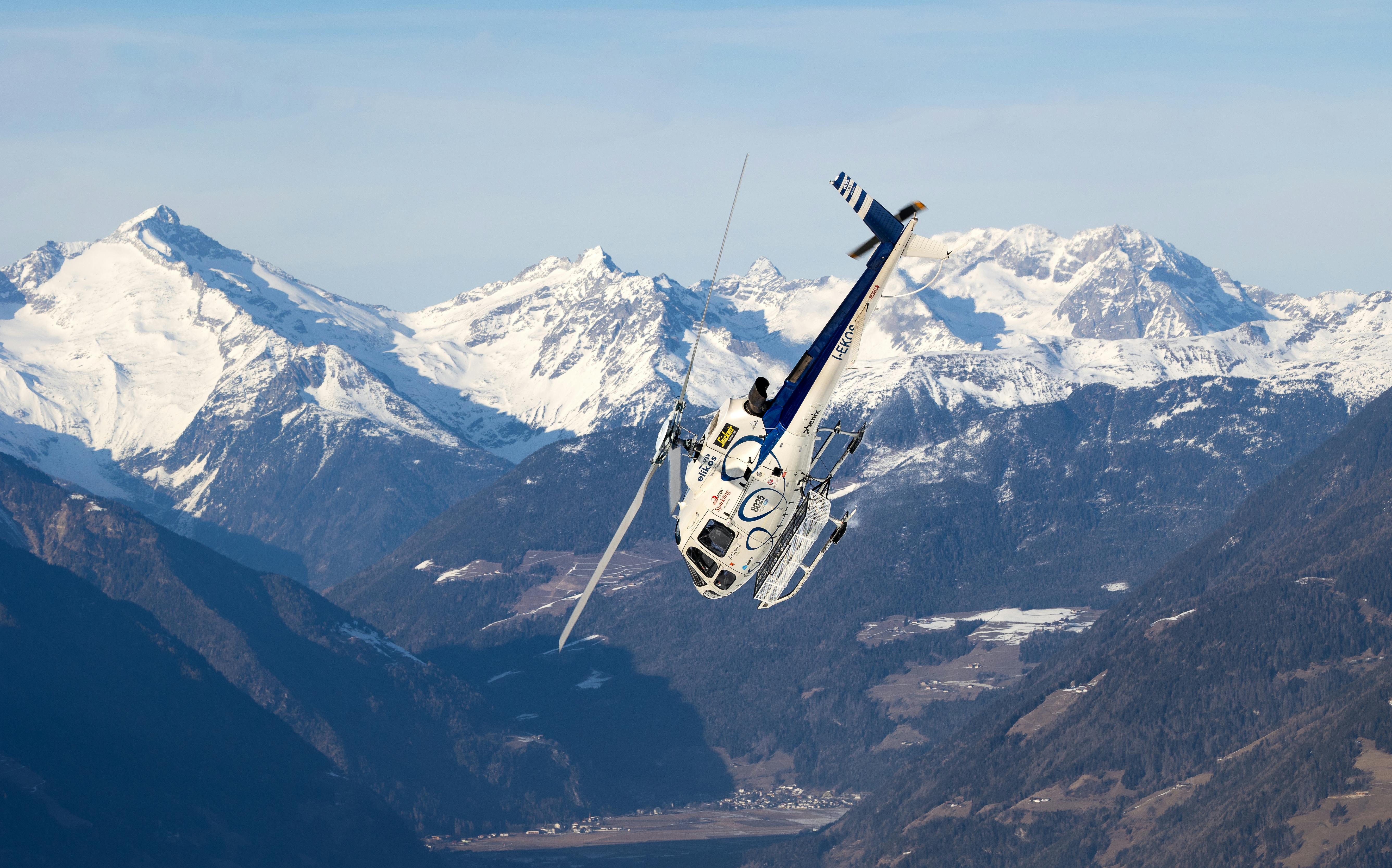 A helicopter flies over the scenic snowy Dolomites in Trentino-South Tyrol, Italy, showcasing winter mountain landscapes.