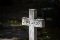 A solemn tombstone in a cemetery featuring a cross with the inscription 'Jezus Alleen' set in a tranquil outdoor setting.
