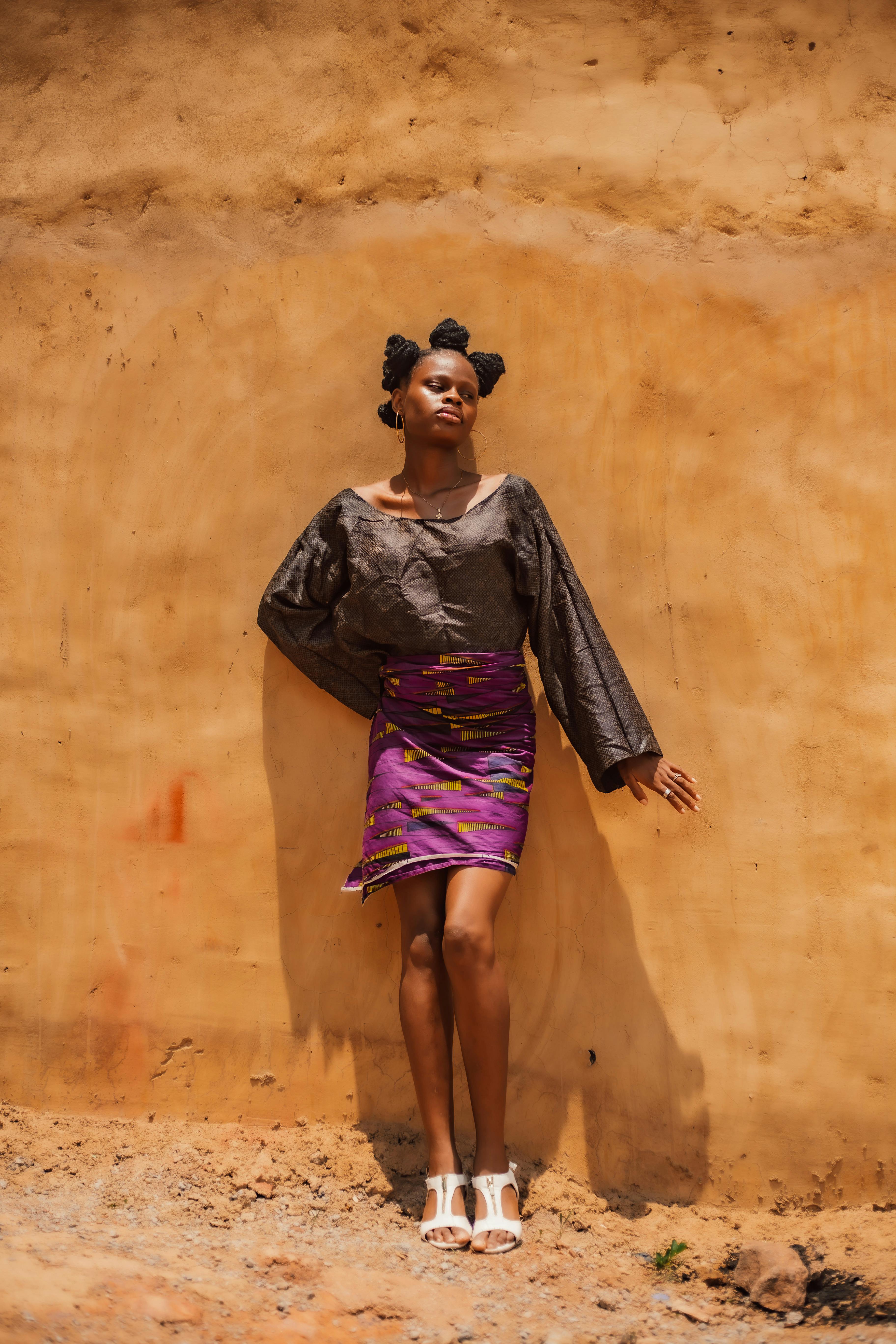 Elegant woman in vibrant attire standing against a rustic wall outdoors.