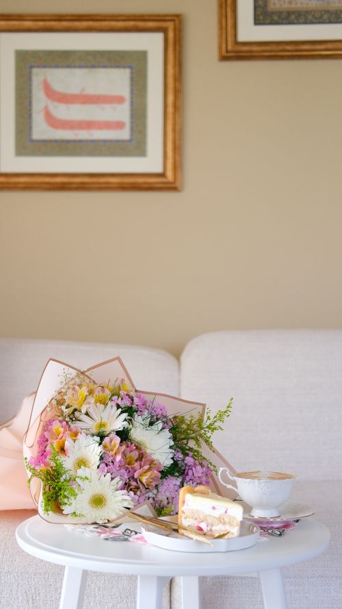 Free A cozy indoor setting featuring a bouquet of flowers, cake slice, and cup on a small table. Stock Photo
