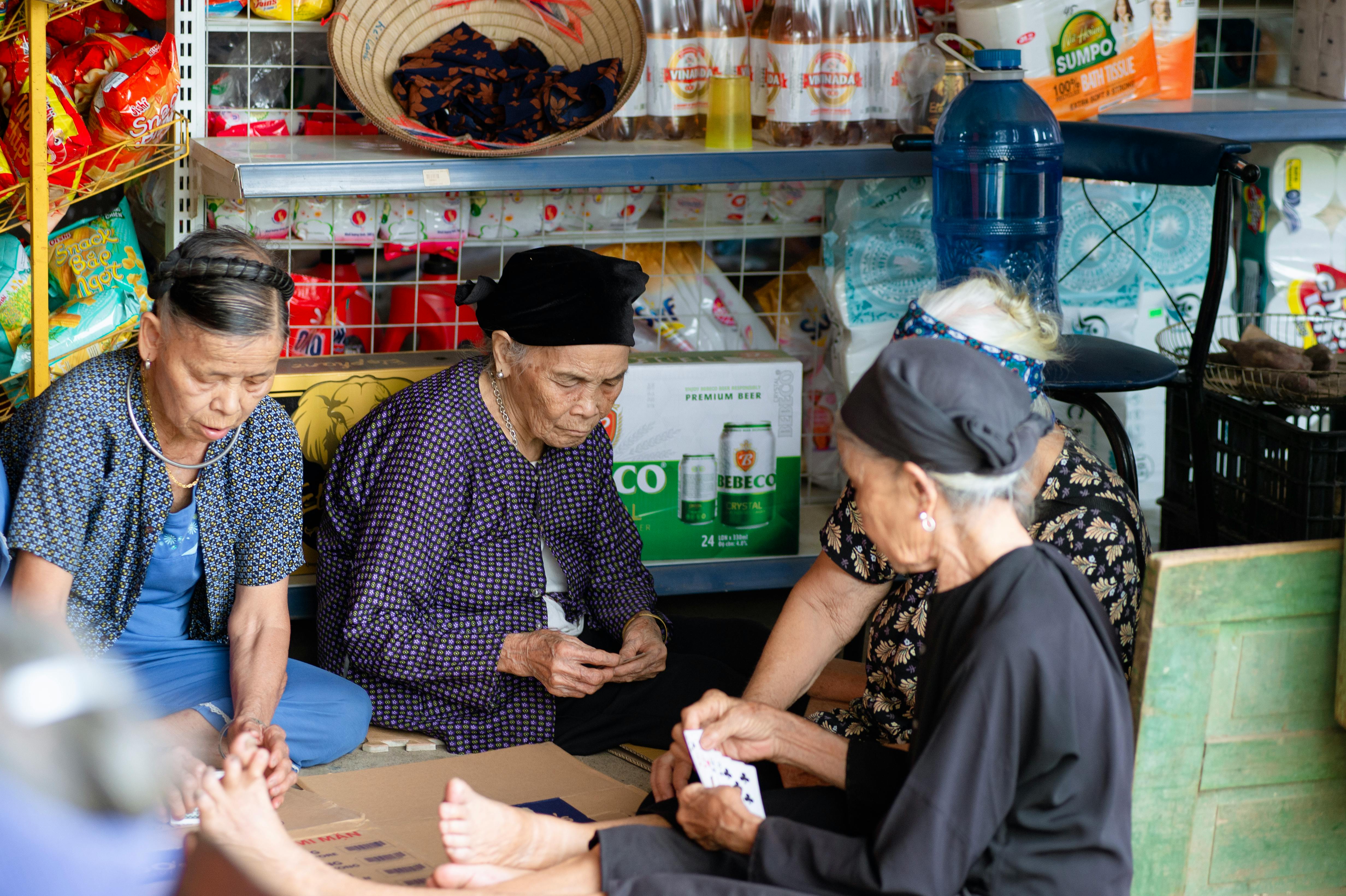 A group of elderly women playing cards in a traditional Vietnamese market setting, Ha Giang, Vietnam.