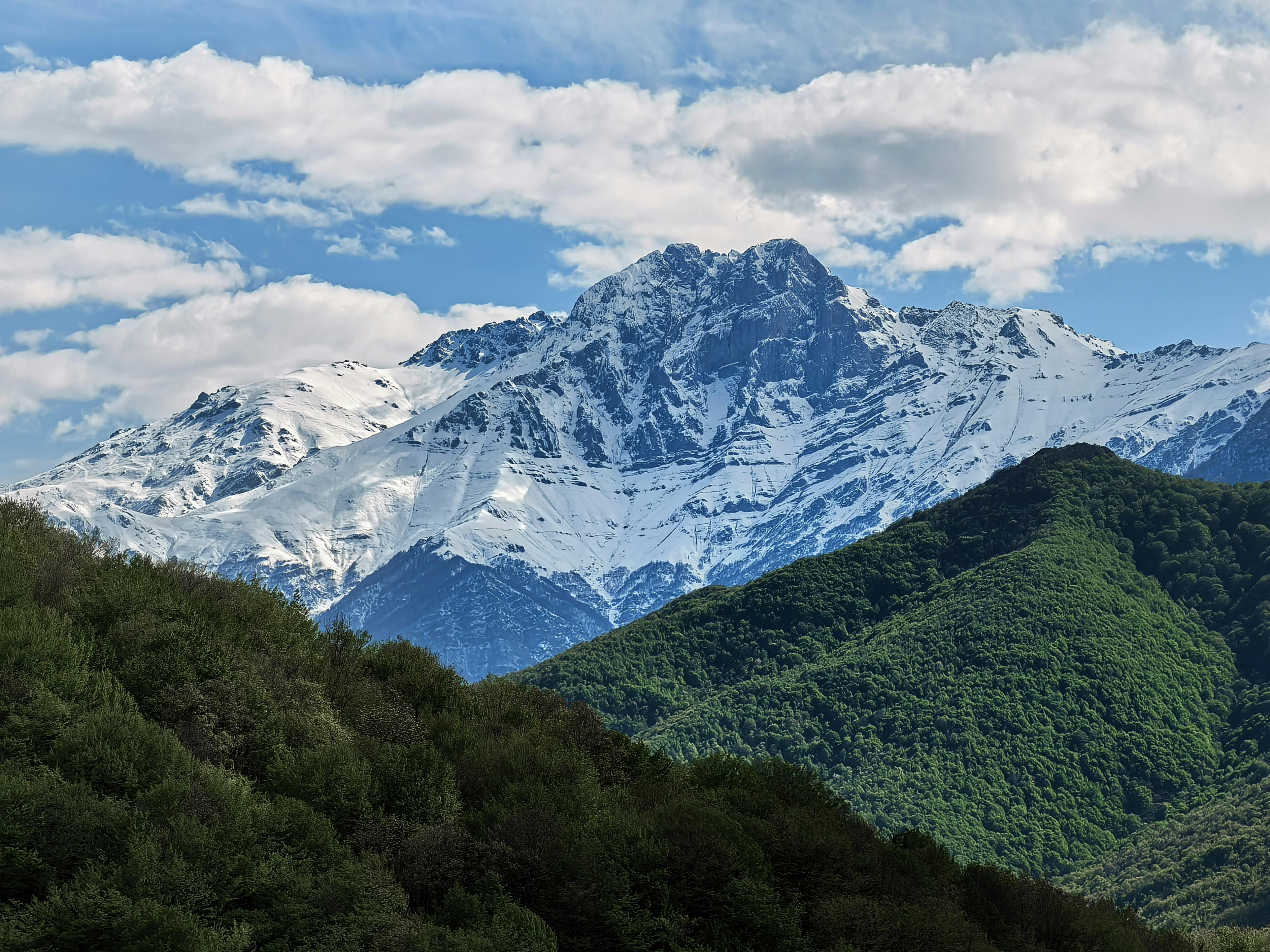 Stunning view of a snow-capped mountain against a blue sky and green foreground hills.