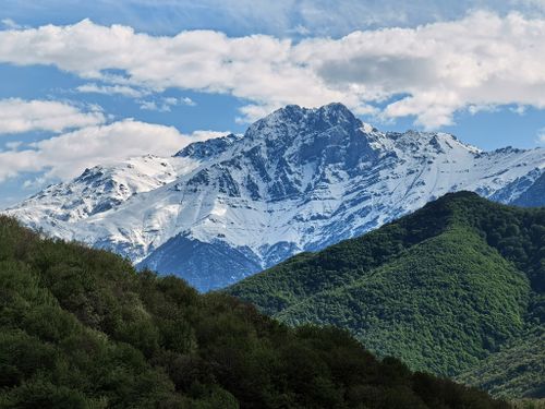 Free Stunning view of a snow-capped mountain against a blue sky and green foreground hills. Stock Photo