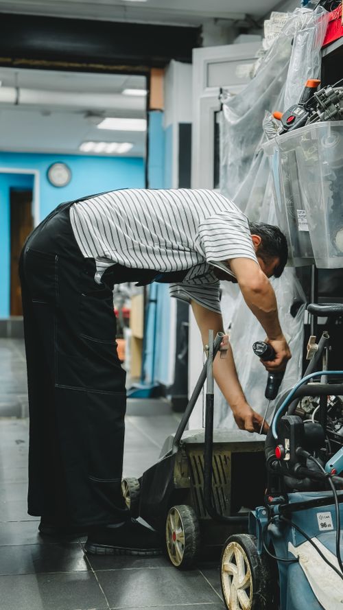 Free A person fixing a lawn mower in a workshop using a cordless drill. Stock Photo