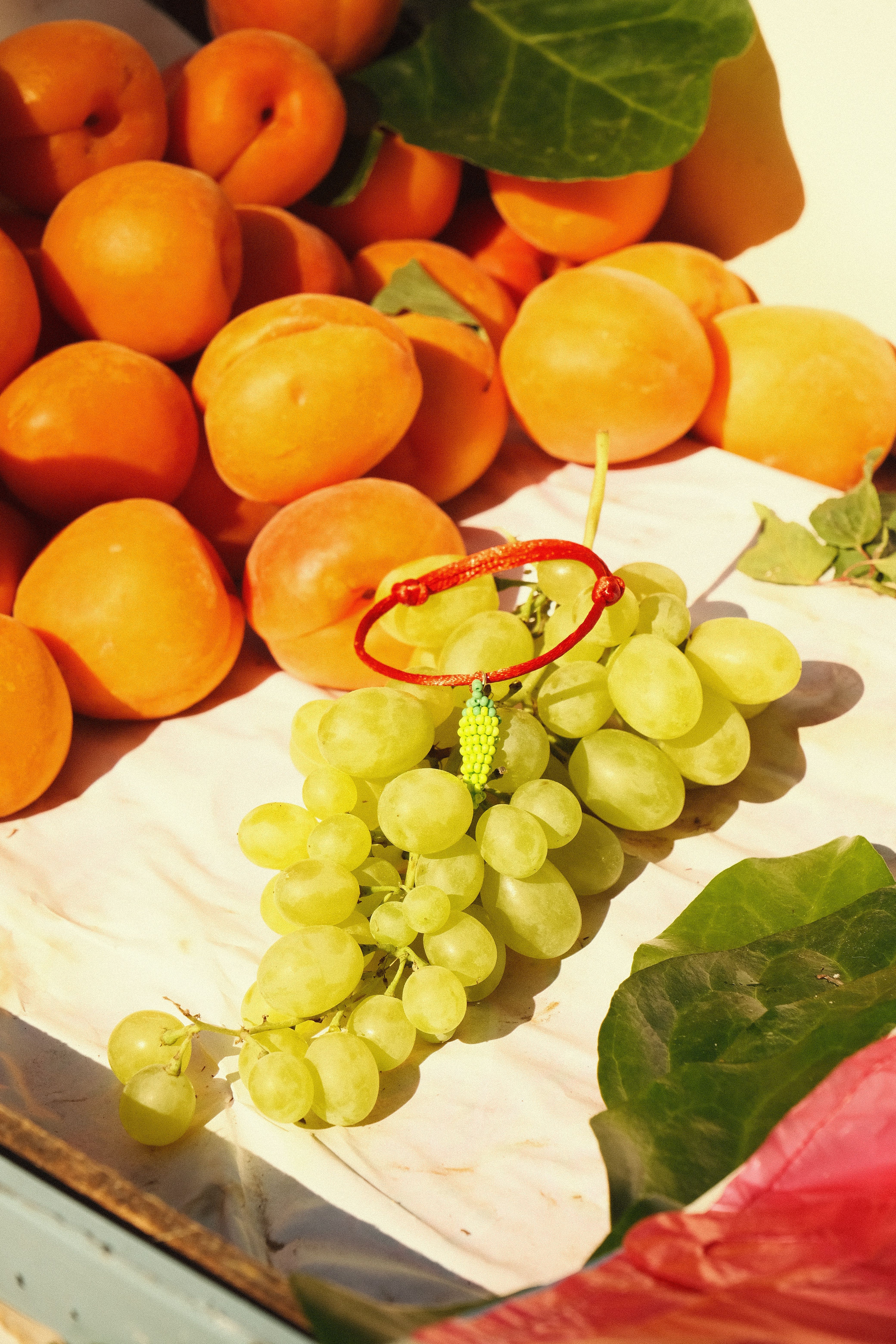 Close-up of fresh apricots and grapes with a red bracelet in sunlight.