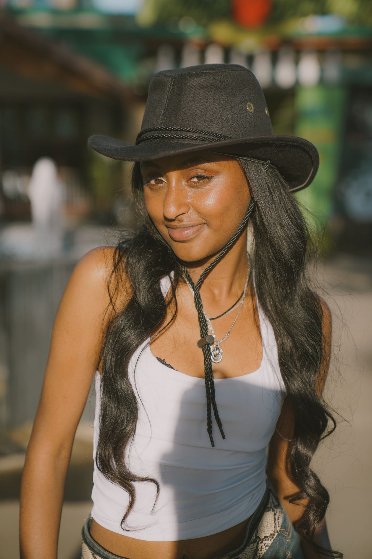 Close portrait of a young woman wearing a dark cowboy hat with a chin cord