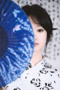 Half face portrait with blue fan, calligraphy background, traditional attire. — photo by Mang Yu