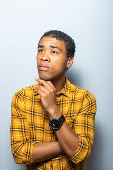 一名身穿黄色格子衬衫的年轻人若有所思地抬起头，他手上戴着一只时尚手表