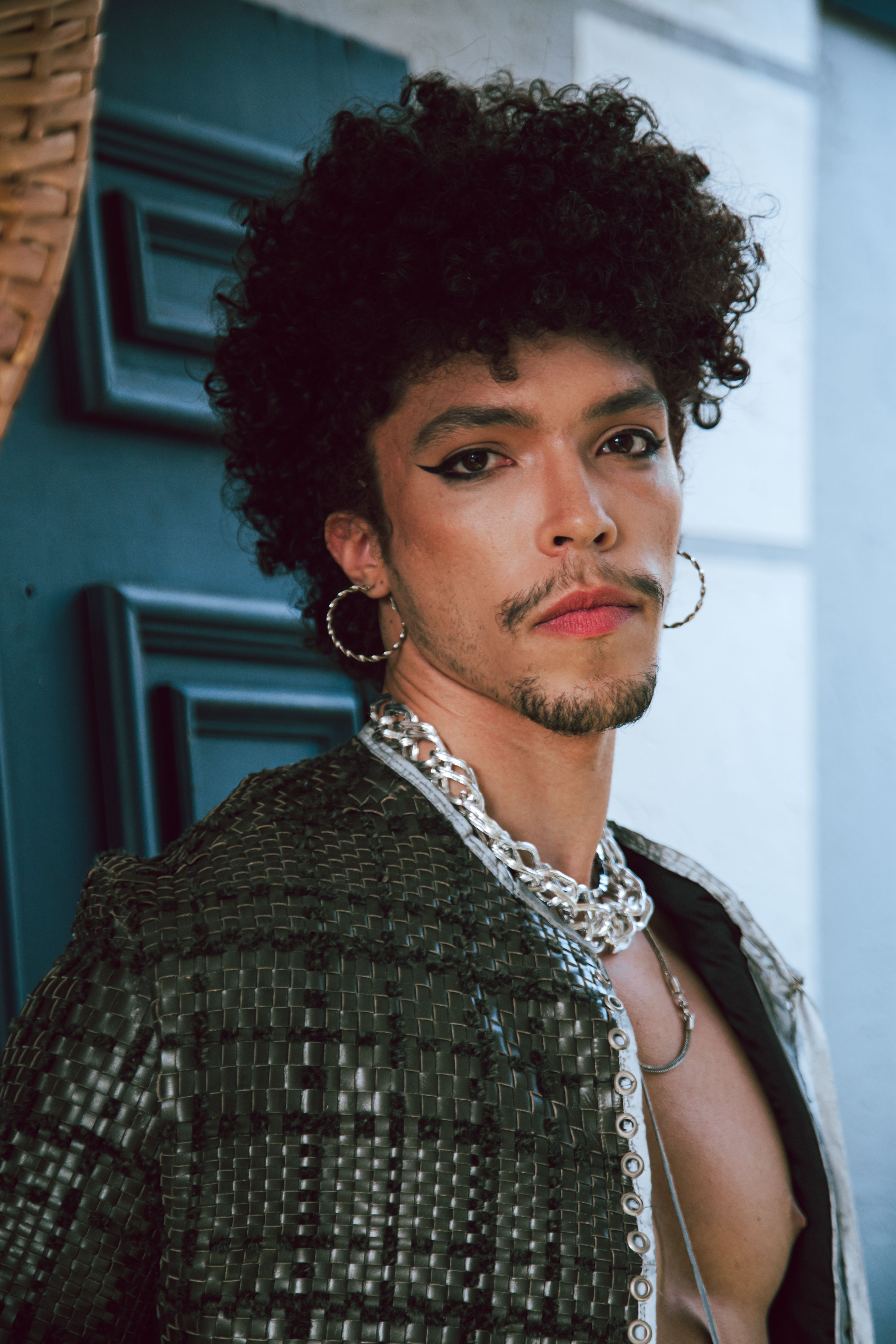 Chic portrait of a person with curly hair, hoop earrings, and bold fashion.