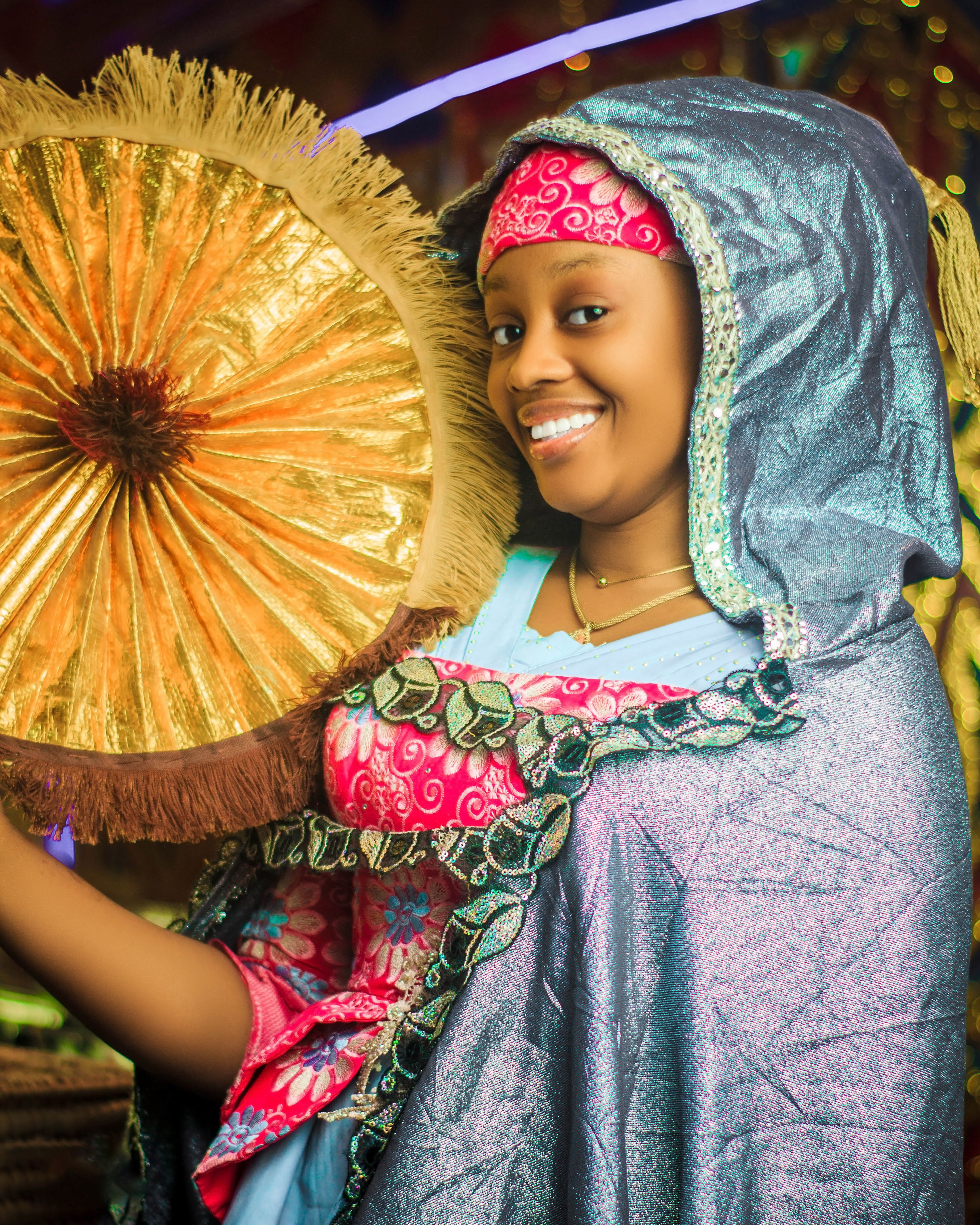 Vibrant portrait of a woman in traditional attire holding a decorative fan indoors.