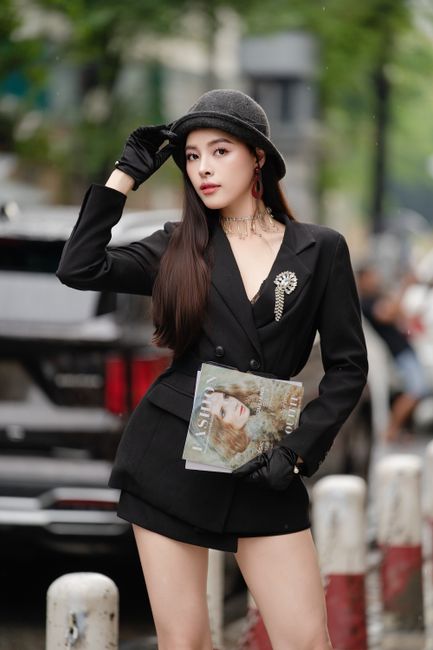 Elegant fashion model in black jacket and hat posing on city street.