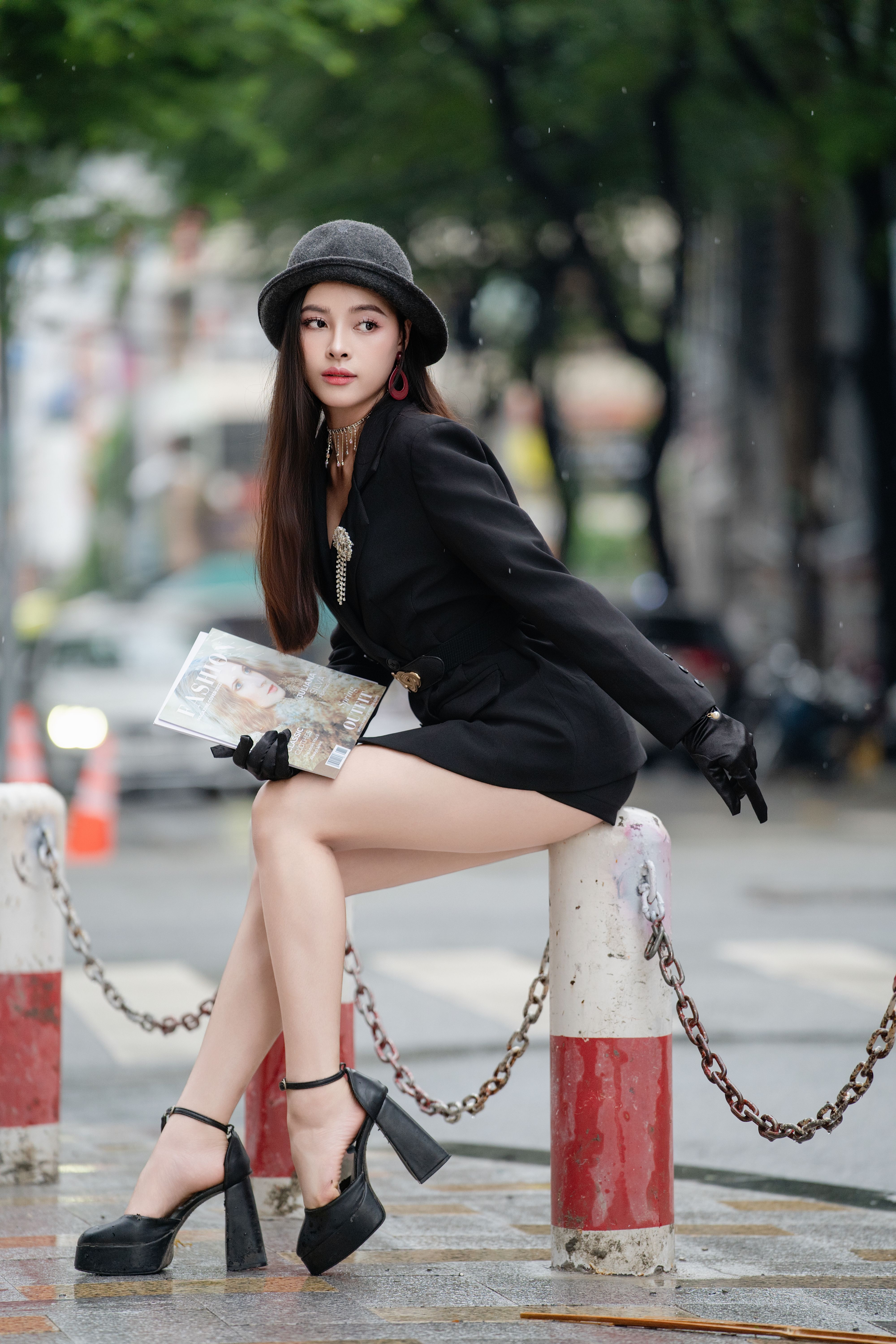 Fashionable woman in black outfit poses outdoors in an urban setting.