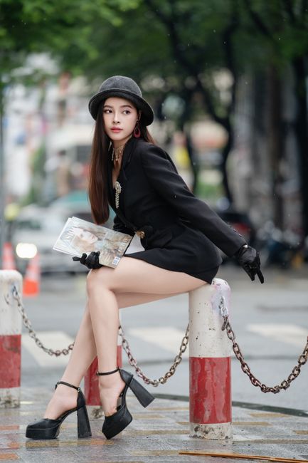 Fashionable woman in black outfit poses outdoors in an urban setting.