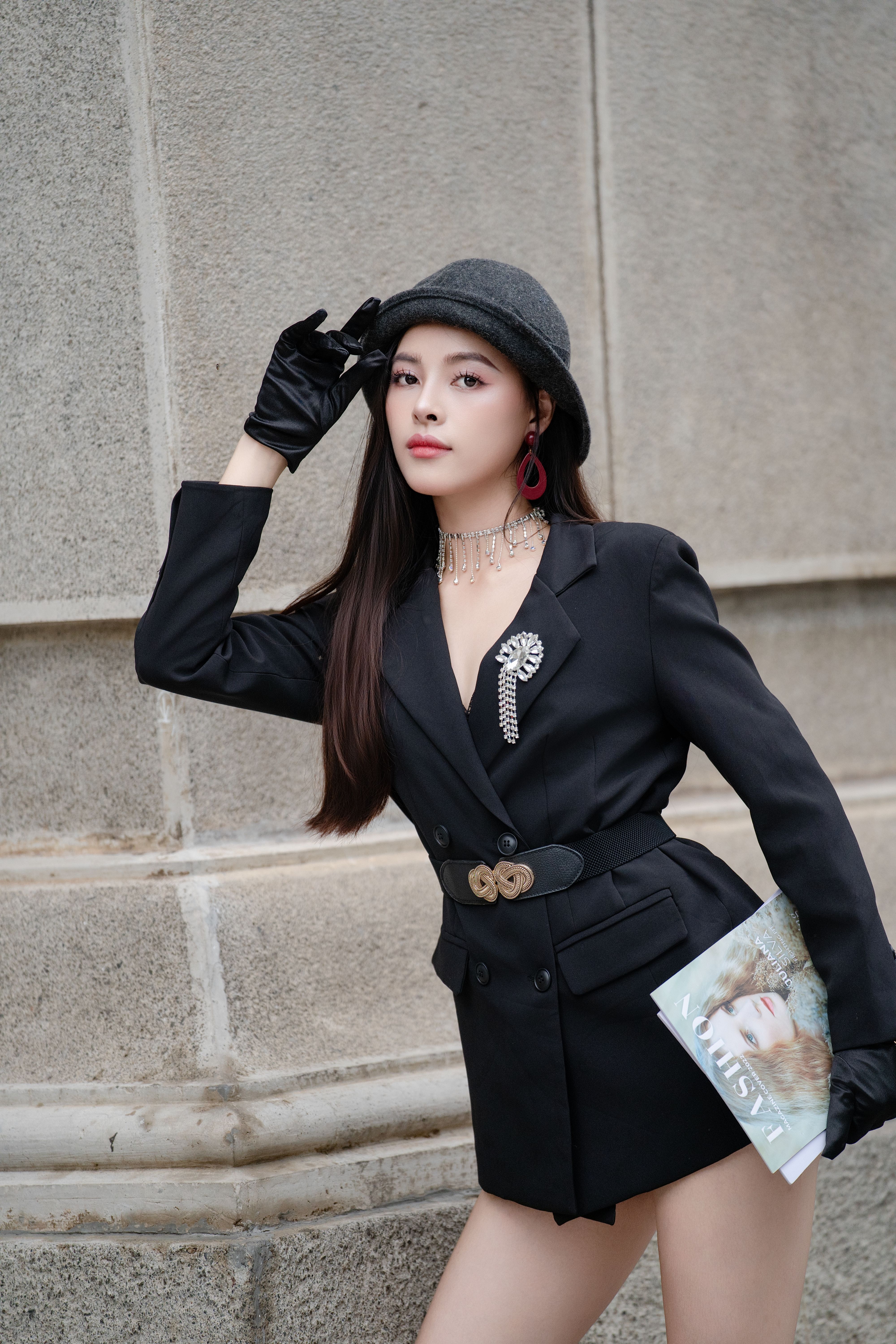 Stylish woman posing in chic black outfit with hat and gloves in urban setting.