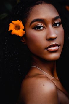 Close-up portrait of a woman with dark hair and orange flower accentuating beauty.