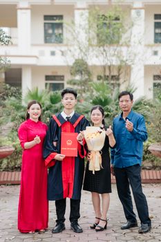 A proud family celebrates a young adult's graduation outdoors with smiles and congratulations.
