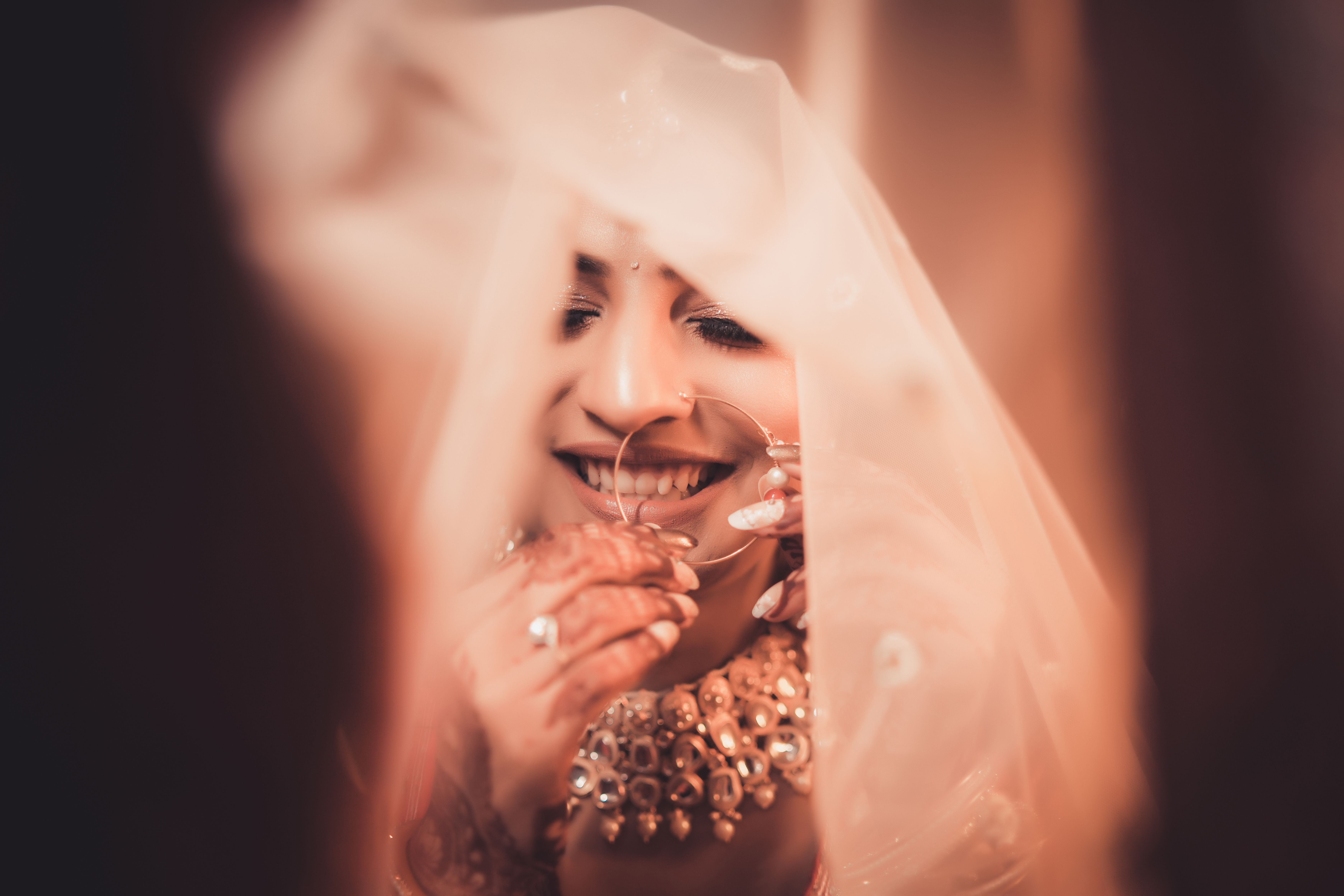 A beautiful bride smiling as she dons traditional jewelry under a delicate veil.