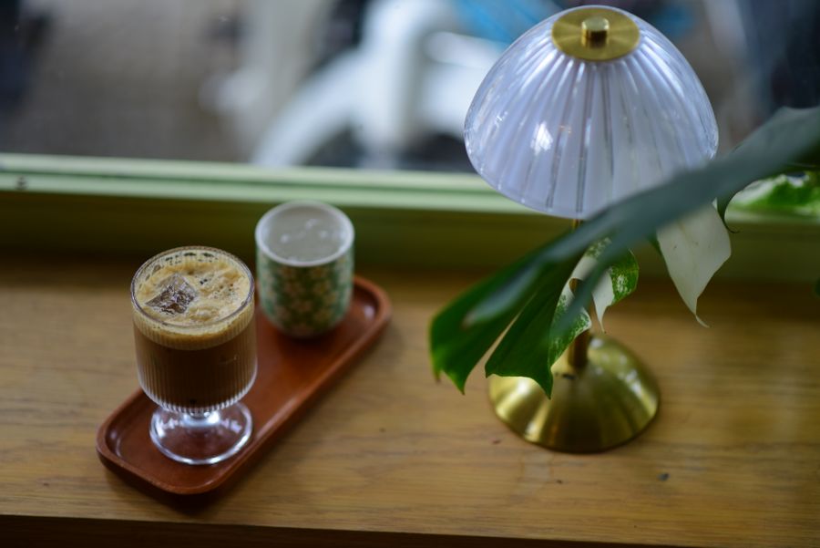 A glass of coffee on a wooden tray under a brass table lamp