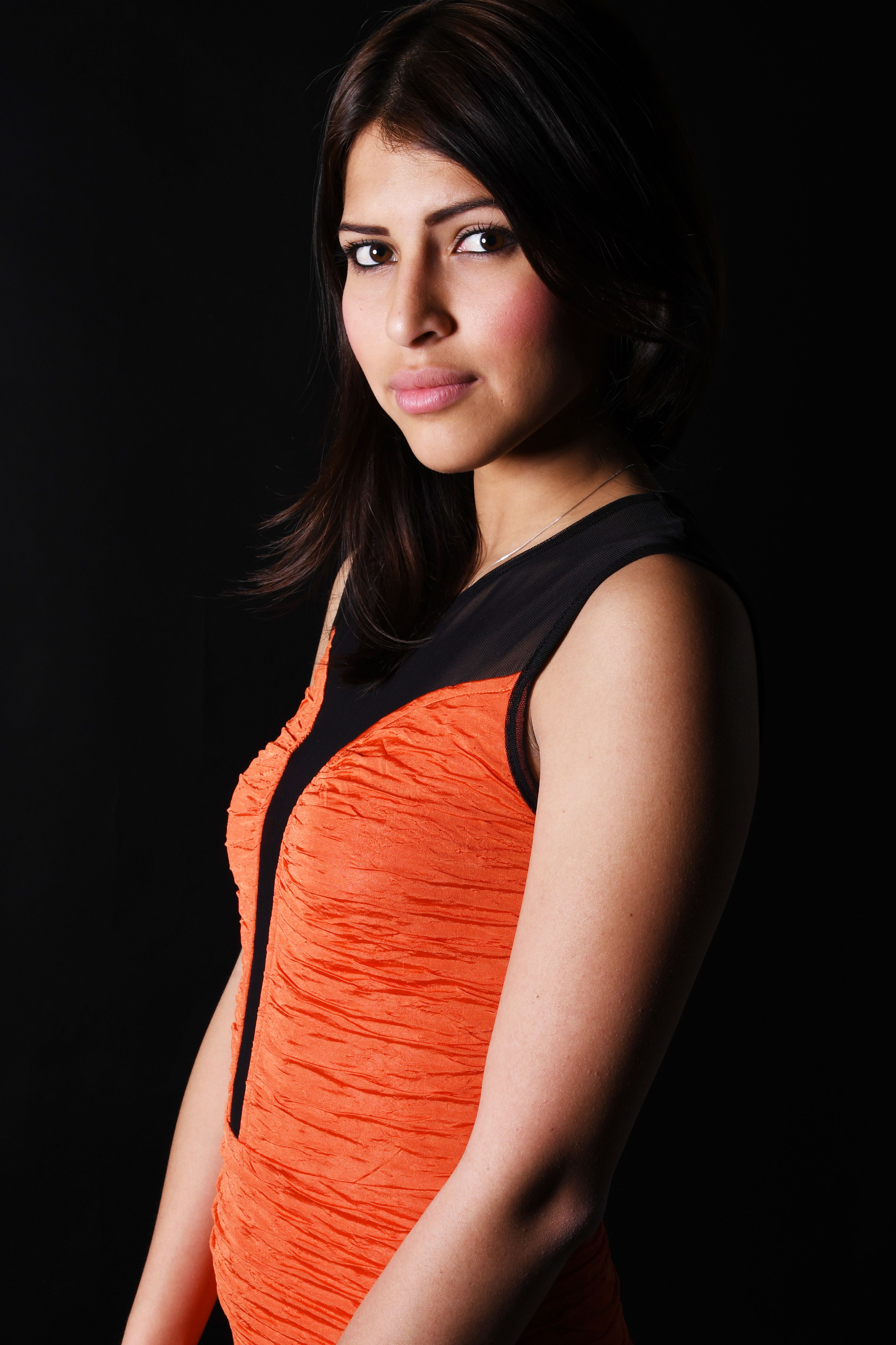 Portrait of a young woman in an orange dress against a dark background, showcasing elegance and style.