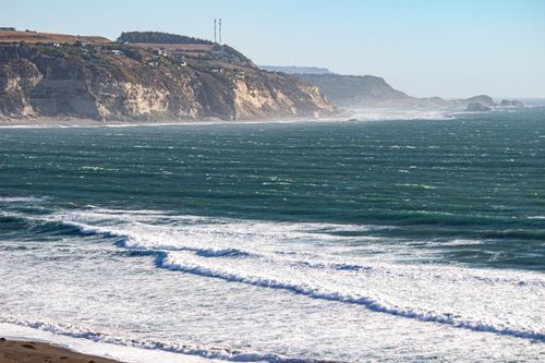 Free Breathtaking coastal view featuring rugged cliffs and expansive ocean waves on a sunny day. Stock Photo