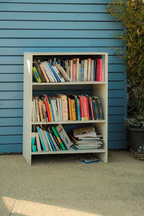 Free Bookshelf filled with various books against a blue wooden wall outdoors. Stock Photo