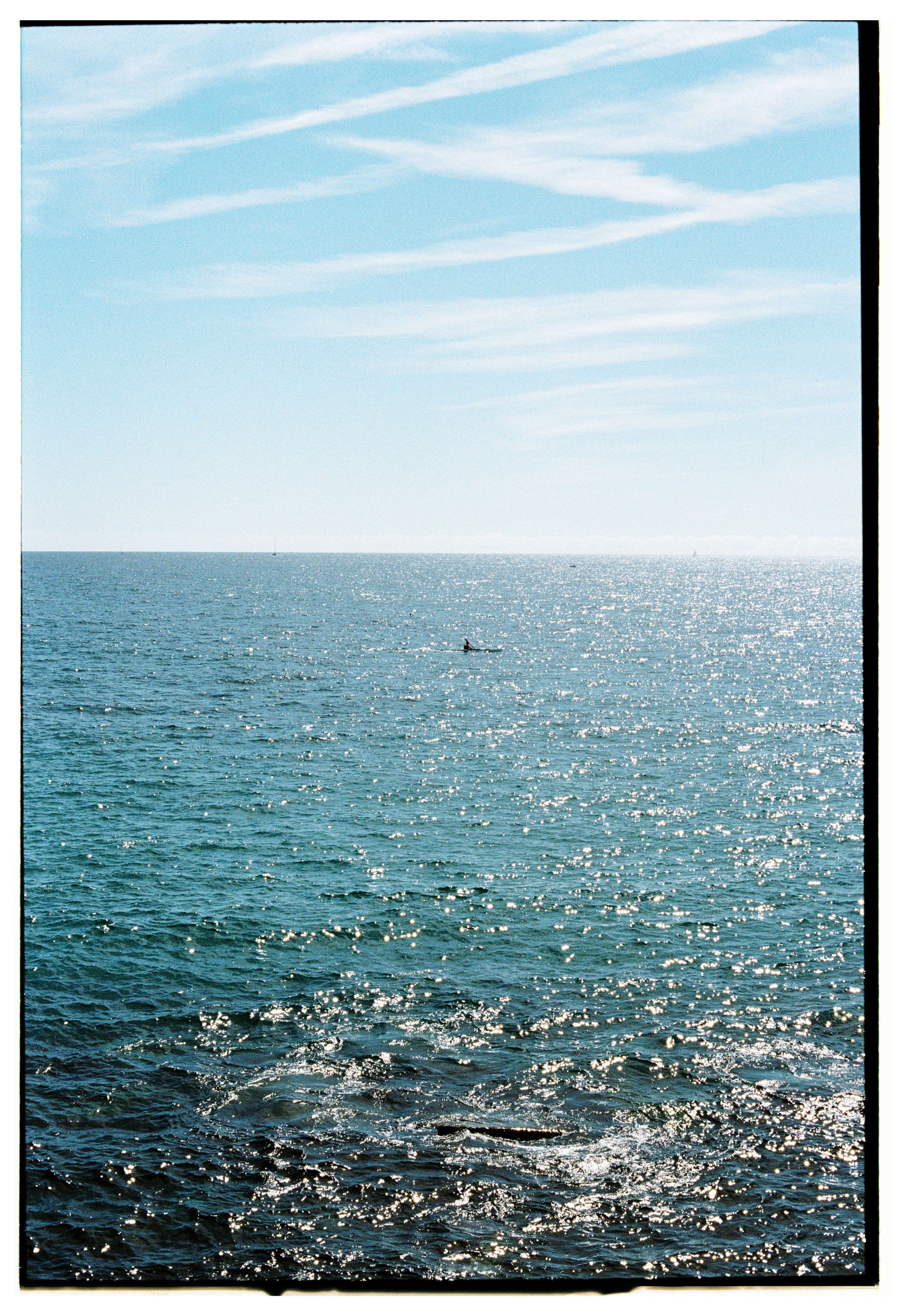 Free Serene ocean scene under a bright blue sky with shimmering sunlight. Stock Photo