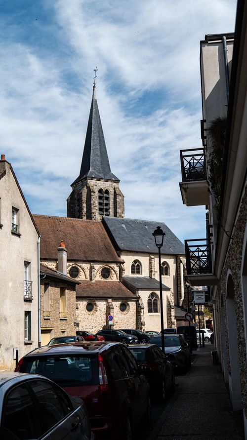 Free Charming street view featuring a historic church with cars parked along a cobblestone path. Stock Photo