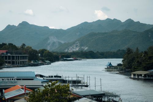 Free Picturesque view of the riverside in Kanchanaburi, Thailand, with mountains in the background. Stock Photo