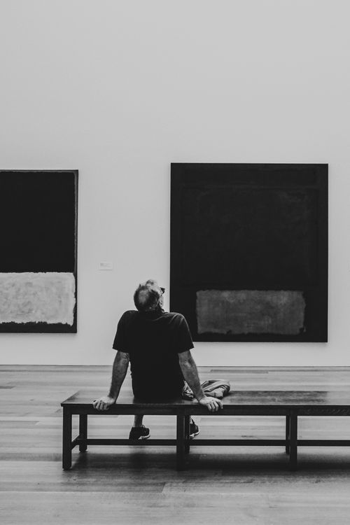 Free A man sits on a bench, contemplating abstract paintings in a gallery. Stock Photo