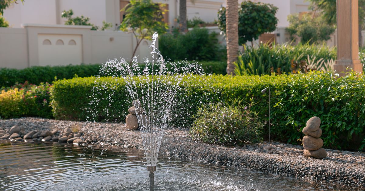 Tranquil garden scene featuring a water fountain in a lush pond, with stacked stones, in Dubai.