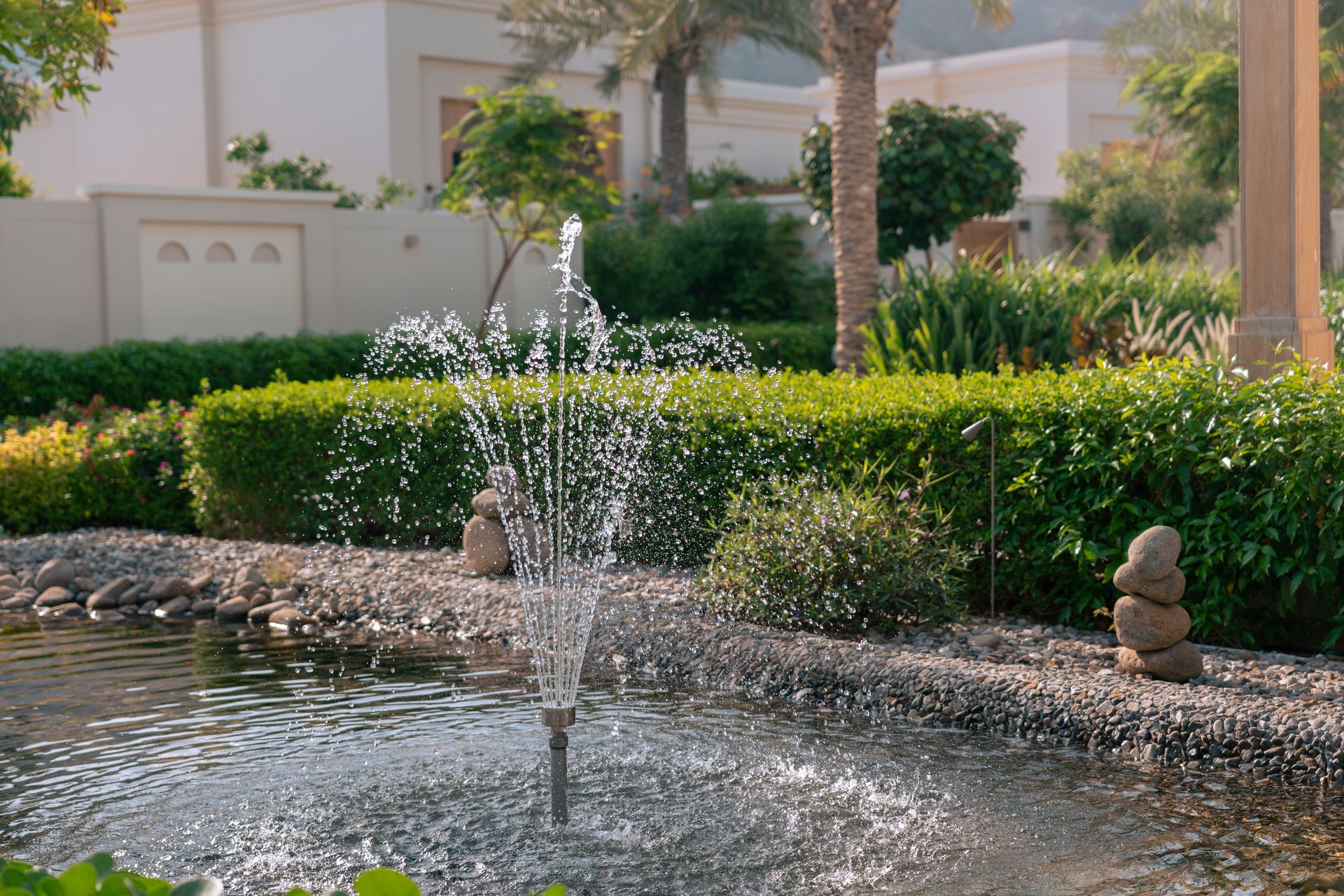 Tranquil garden scene featuring a water fountain in a lush pond, with stacked stones, in Dubai.