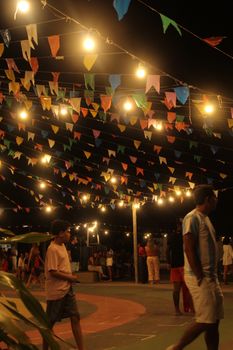 People enjoying a vibrant nighttime festival under string lights and colorful flags.
