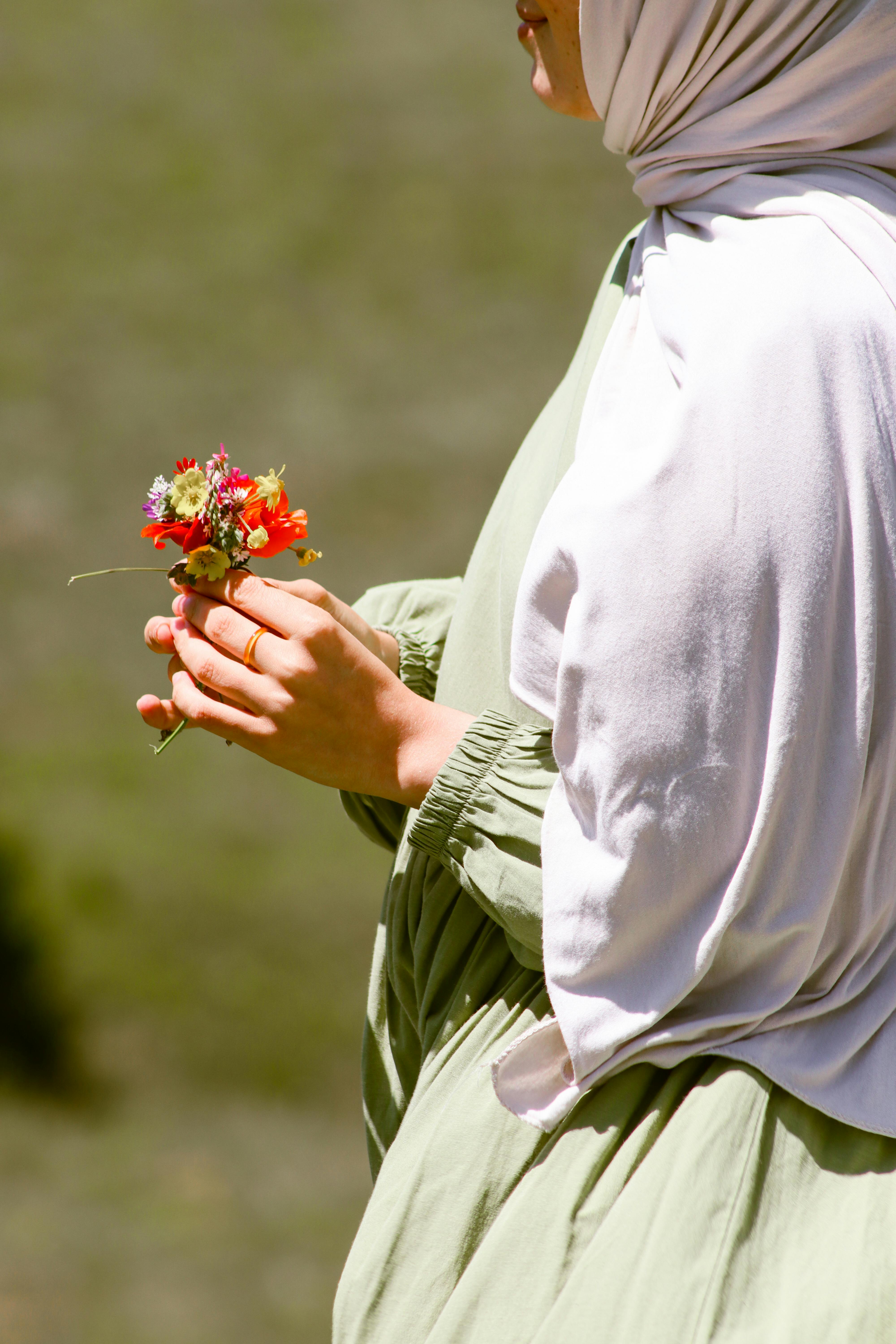 A woman in a green dress holds vibrant wildflowers in sunlight, creating a serene outdoor moment.