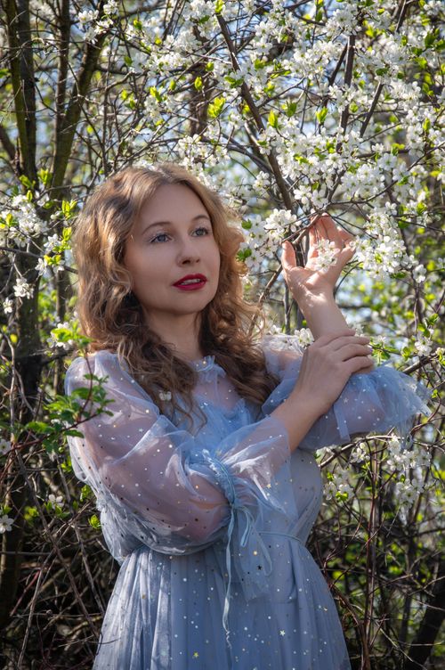 Free A woman in a blue dress enjoying flowering trees in springtime outdoors. Stock Photo
