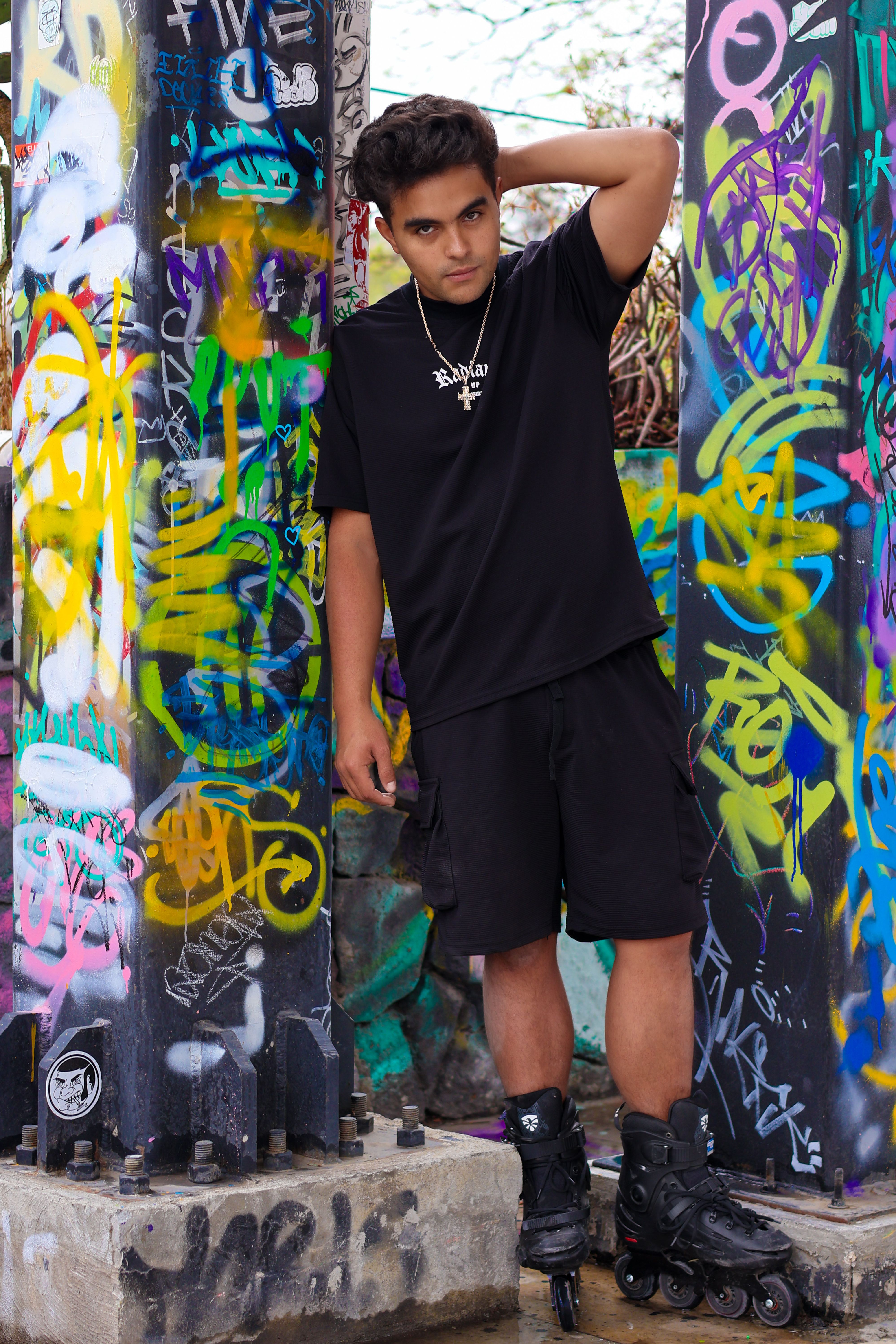 Young man on rollerblades poses in front of a vibrant graffiti-covered wall.