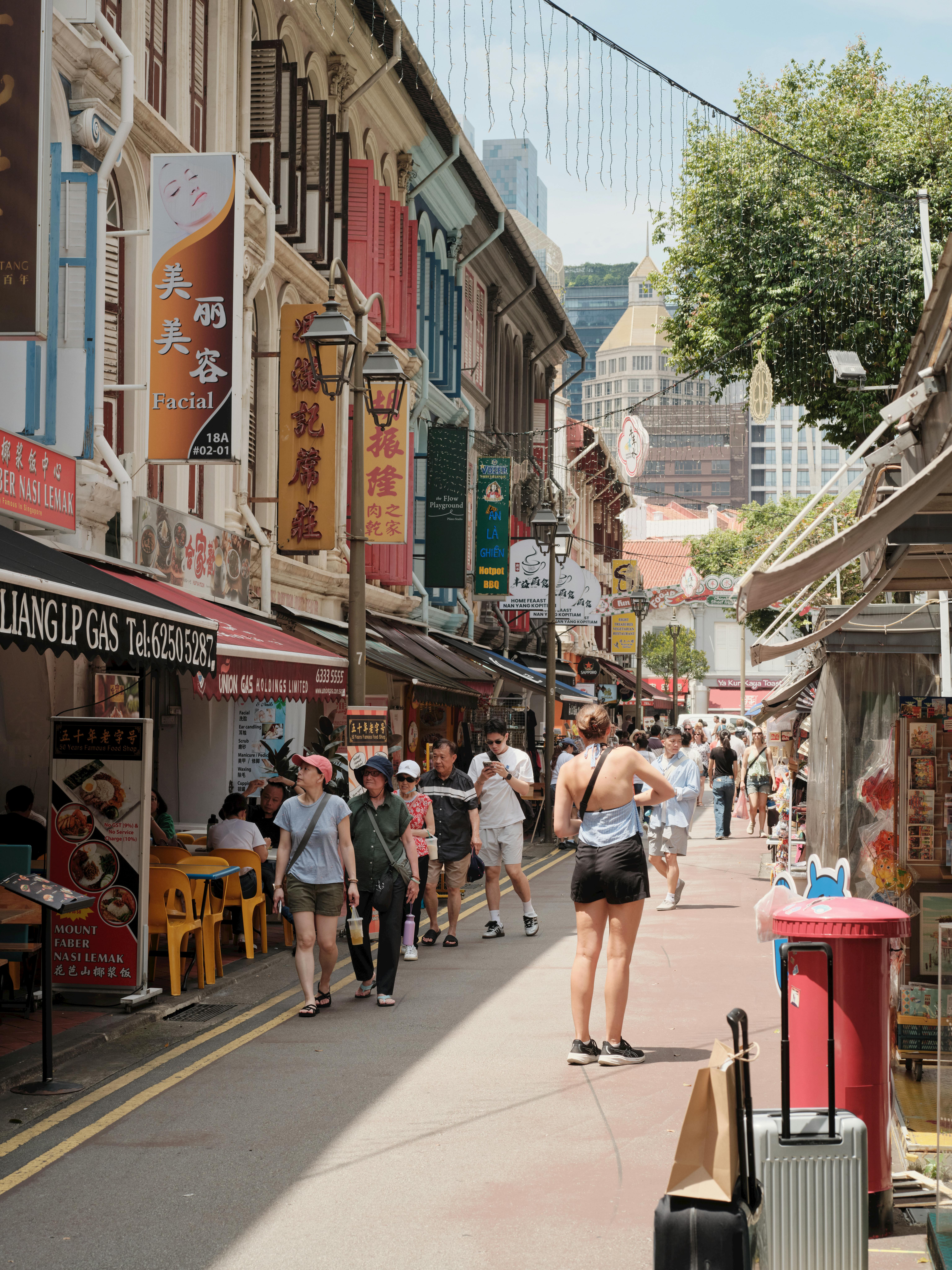 Visitors in casual summer clothing walking past colourful Peranakan shophouses in Singapore's Chinatown district