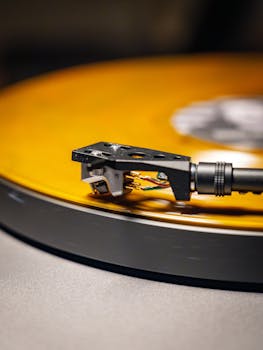 A detailed view of a turntable needle on a spinning yellow vinyl record, showcasing classic music nostalgia.