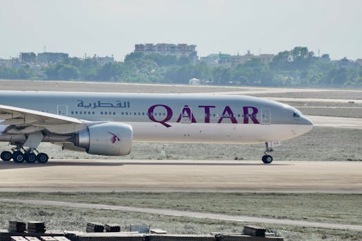 A Qatar Airways aircraft taxiing on the runway with a distant cityscape.