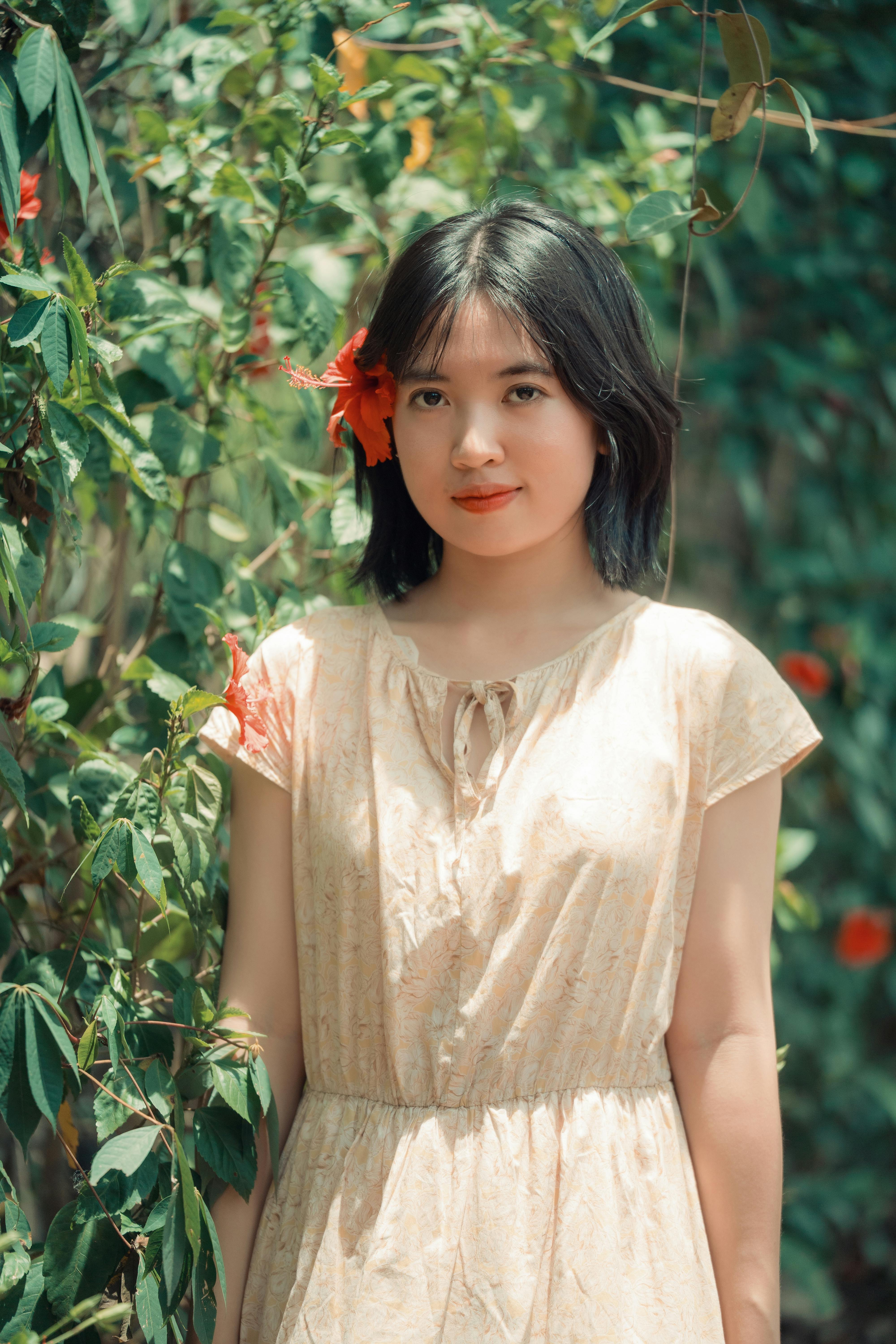 Portrait of a young woman with hibiscus flower, standing amidst vibrant greenery, capturing a summer vibe.
