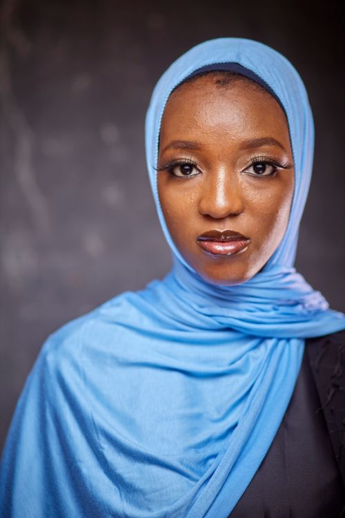 Free A close-up portrait featuring a woman wearing a blue hijab and black clothing, set against a neutral backdrop. Stock Photo