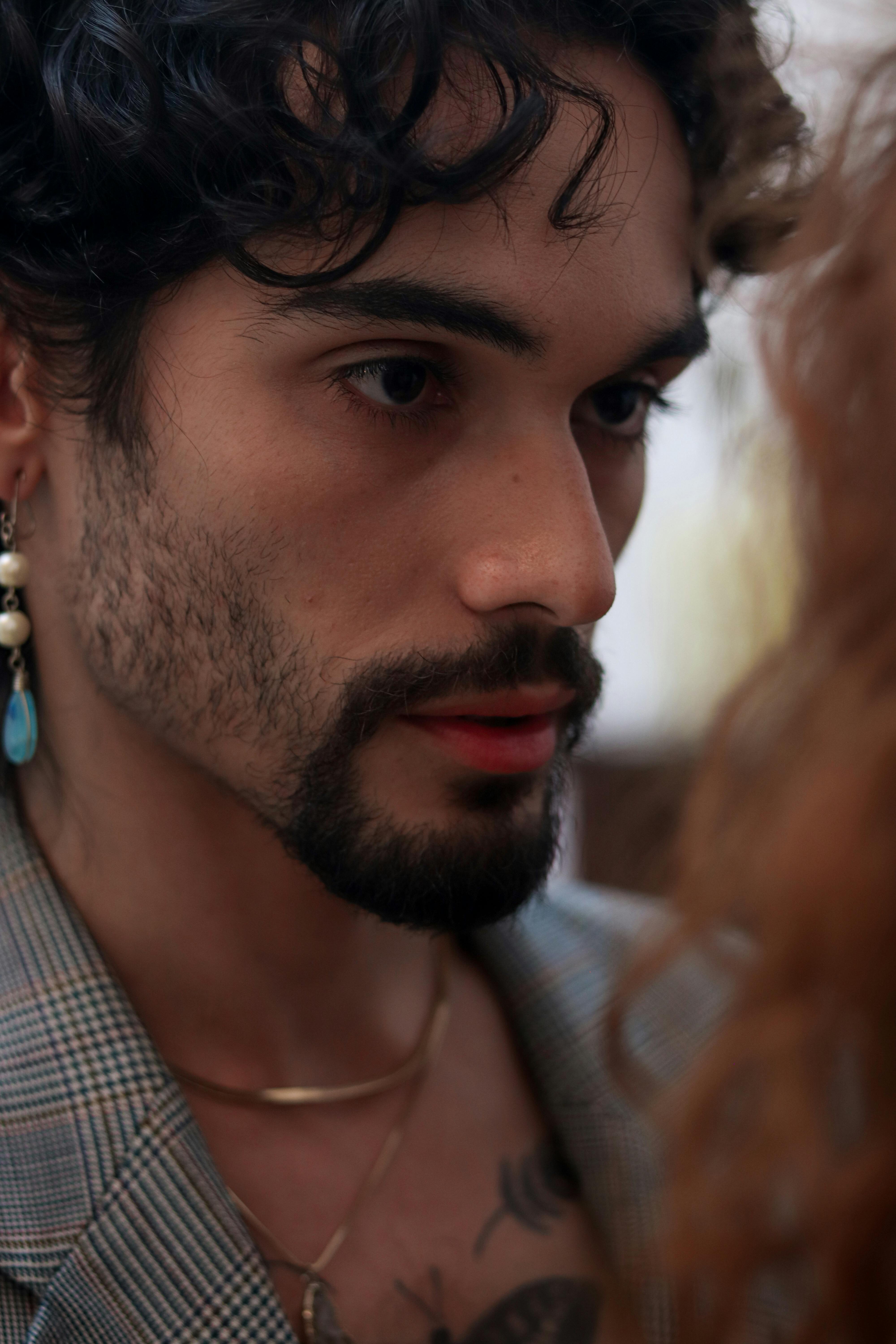Intimate close-up of a young man's profile, wearing earrings and a plaid jacket, showcasing deep emotion.