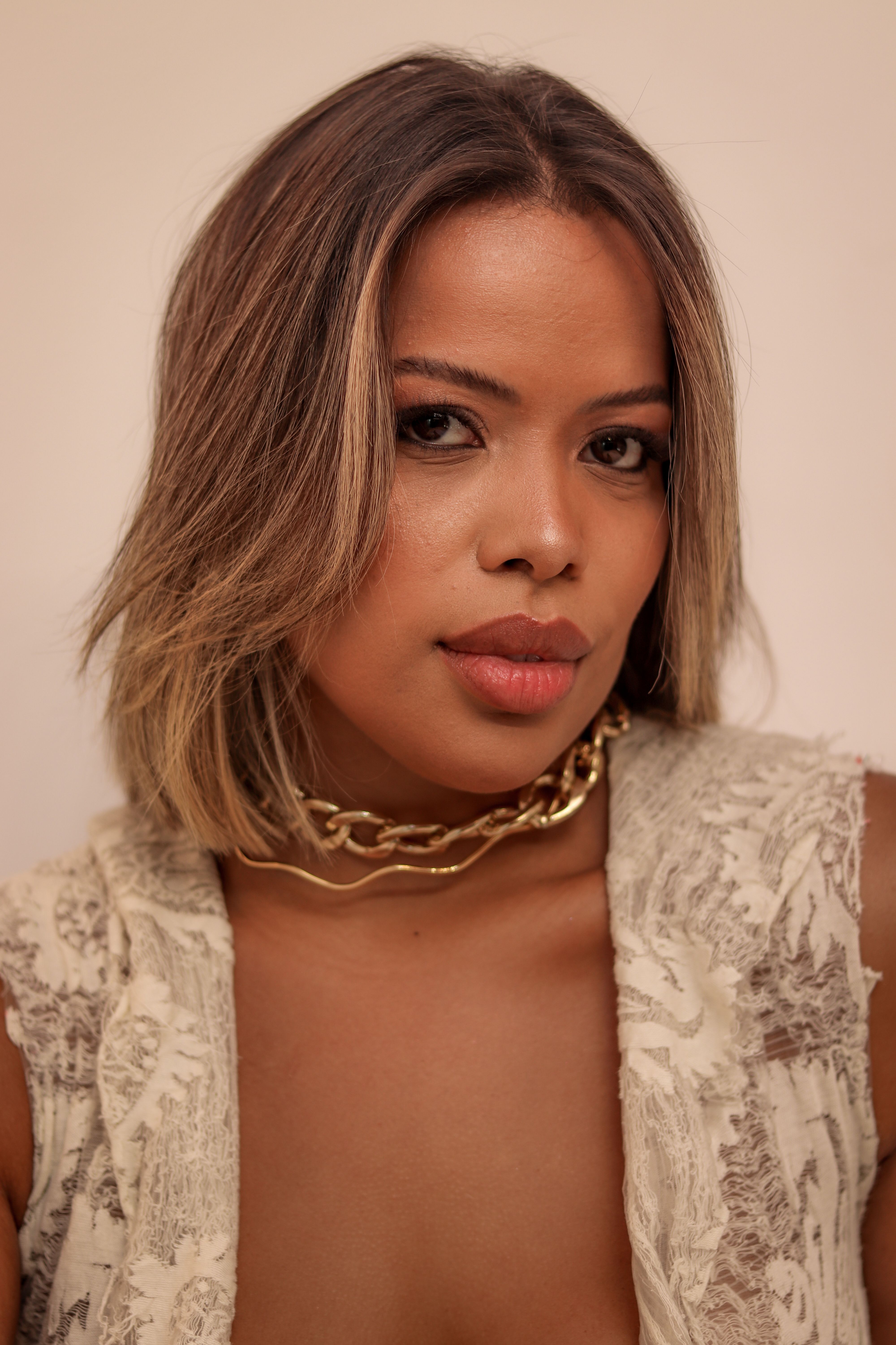Close-up portrait of a woman with short hair, gold jewelry, and a neutral background.