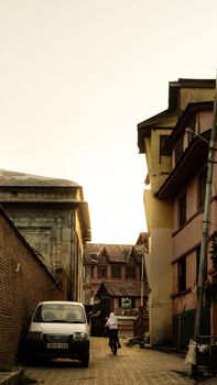 A person rides a bicycle through a narrow alleyway surrounded by rustic architecture at sunset.