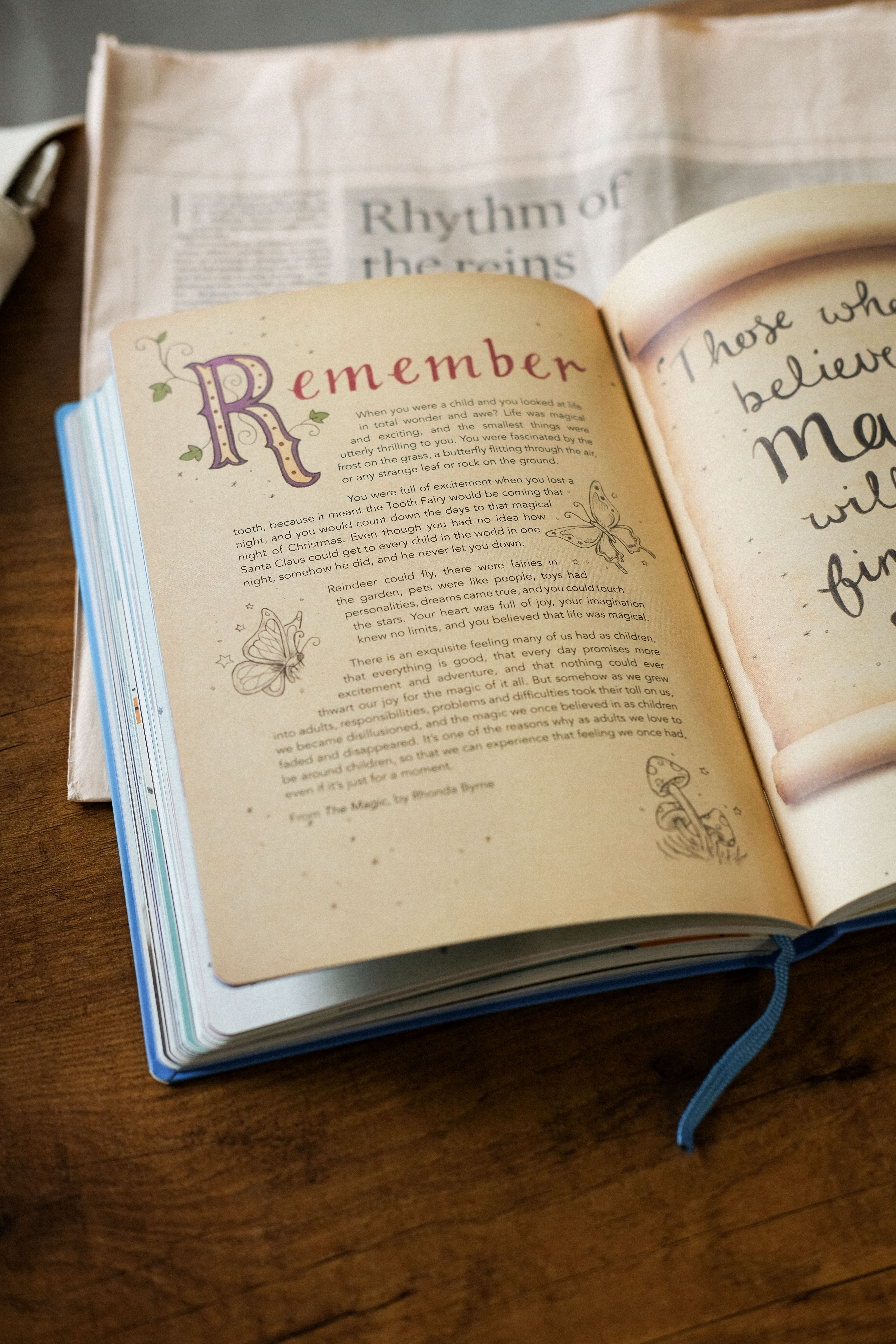 An open book displaying inspiring text, placed on a wooden table beside a newspaper.