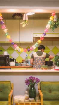 A person is cooking in a decorated kitchen with colorful garlands and a vase of flowers.